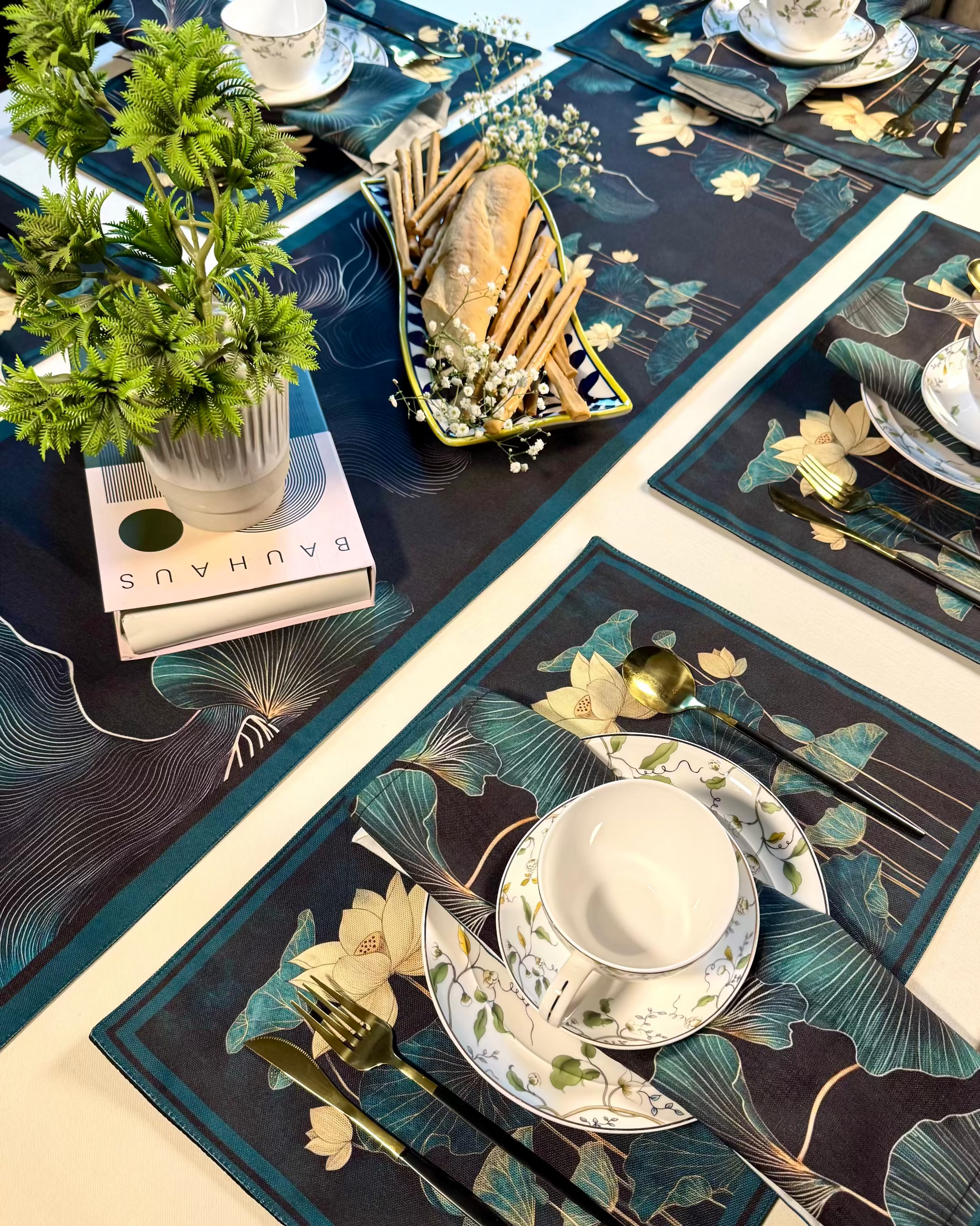 Decorative table setting with floral placemats, cutlery, and a plant on a blue tablecloth.