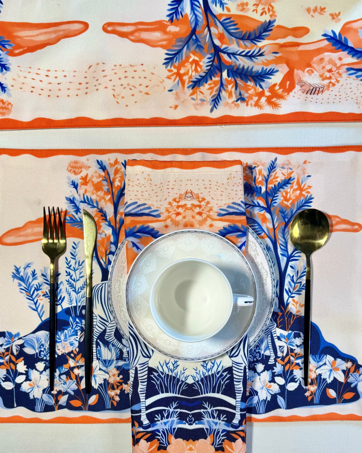 Table setting with a floral-patterned tablecloth, white cup and saucer, and decorative cutlery.